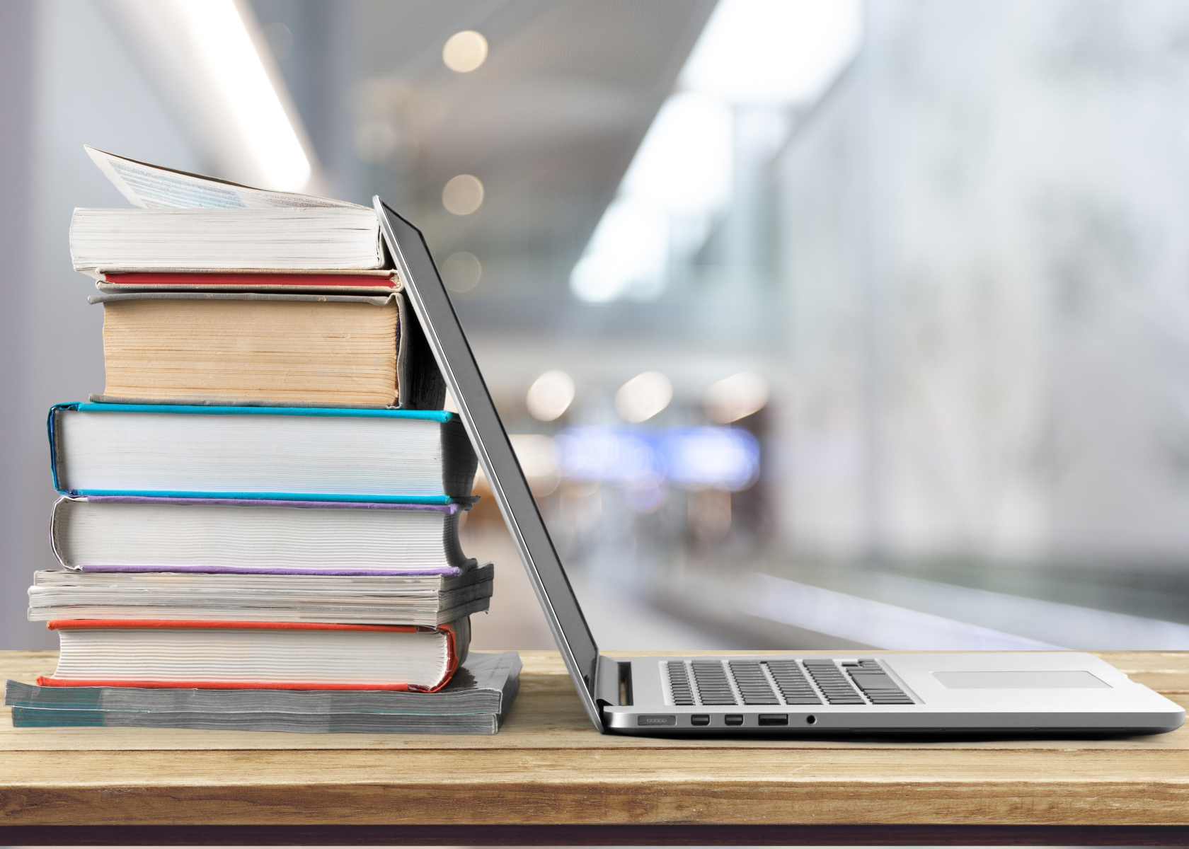 Stack of books with laptop on wooden table