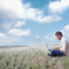 ann mit Laptop auf Wiese vor blauem Himmel