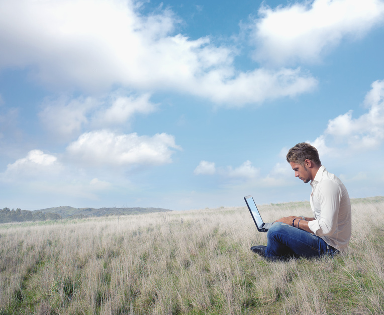 ann mit Laptop auf Wiese vor blauem Himmel