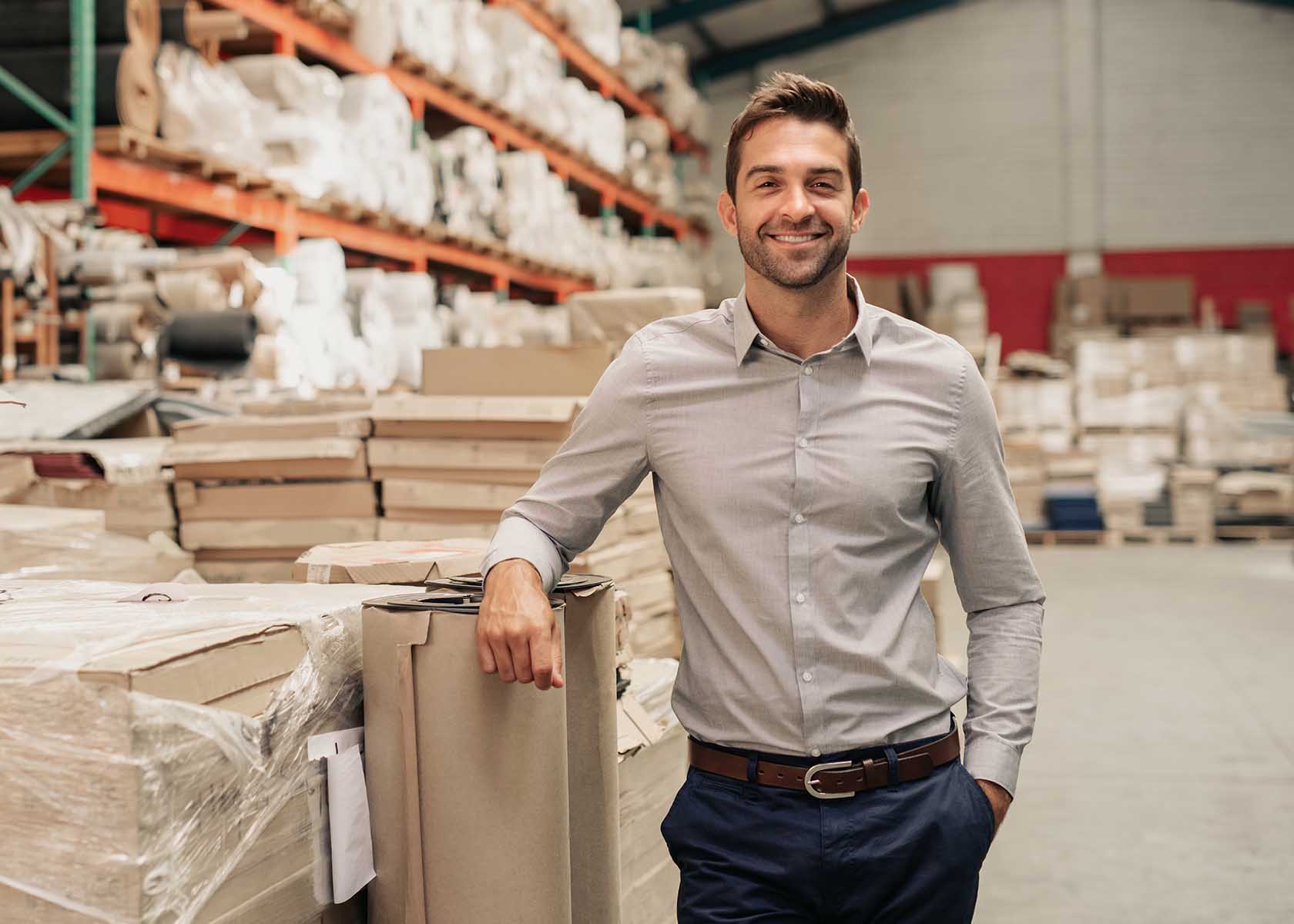 Manager smiling while leaning against stock in a large warehouse