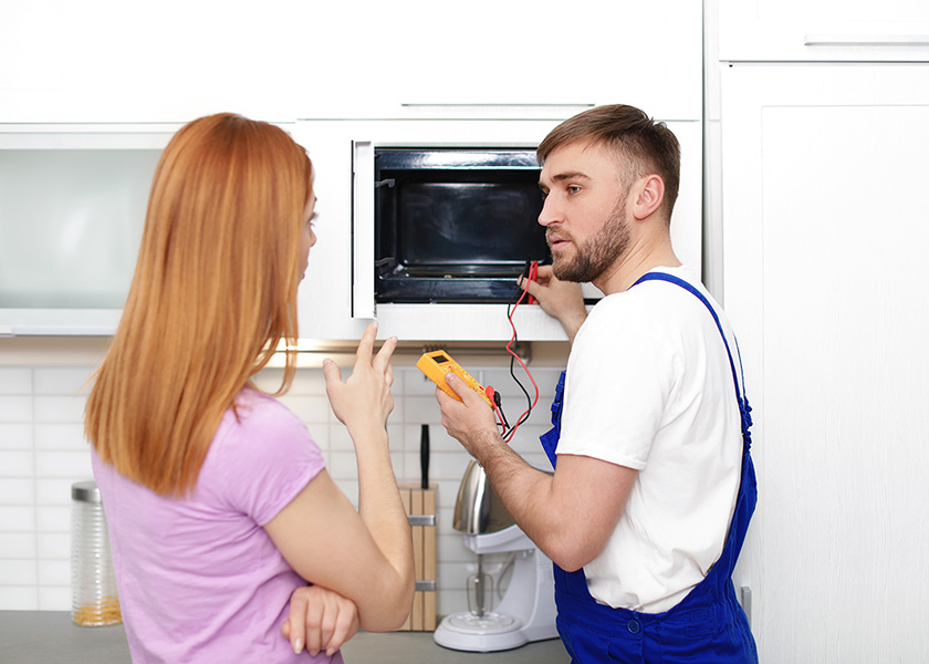 Housewife and repairman near microwave oven in kitchen