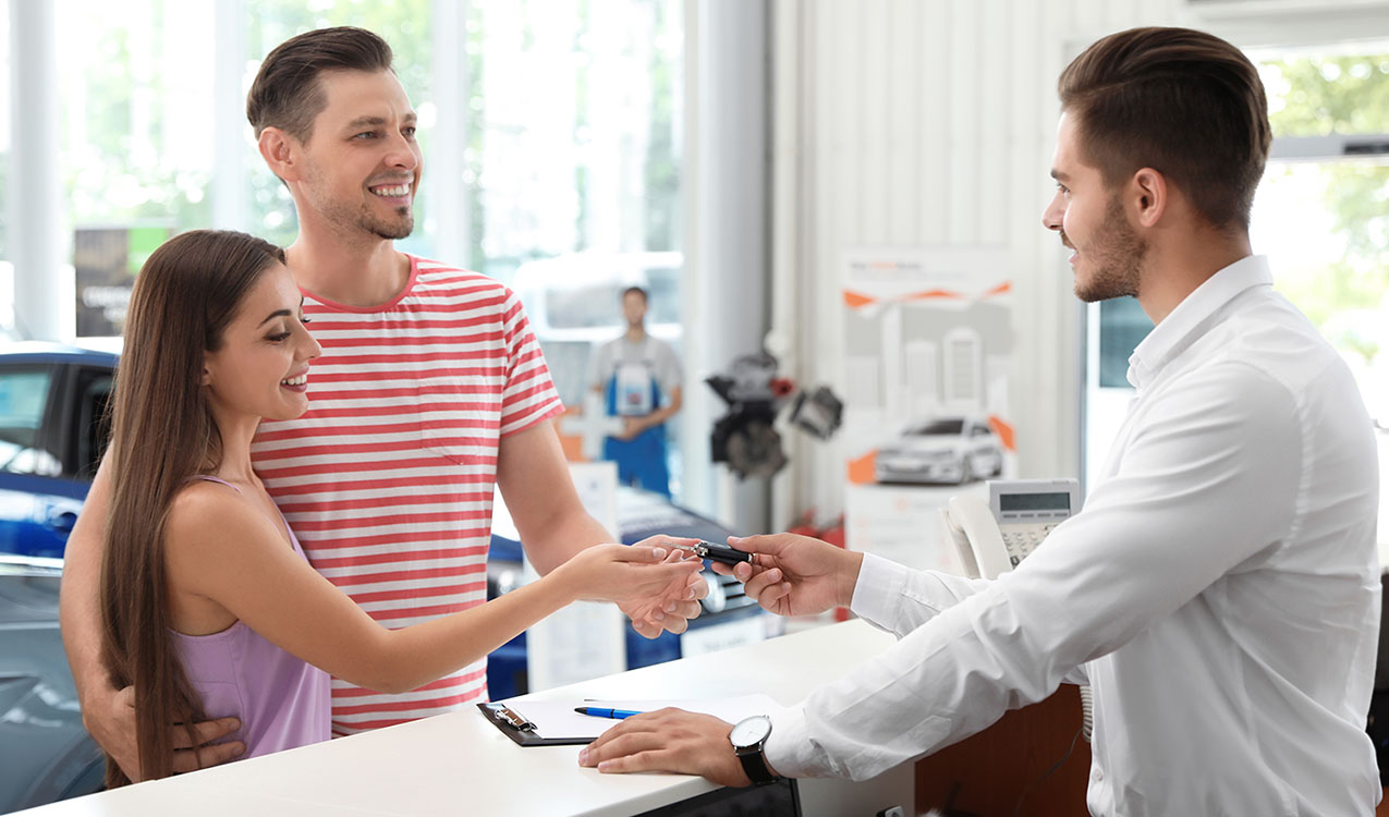 Salesman giving car key to happy couple in salon